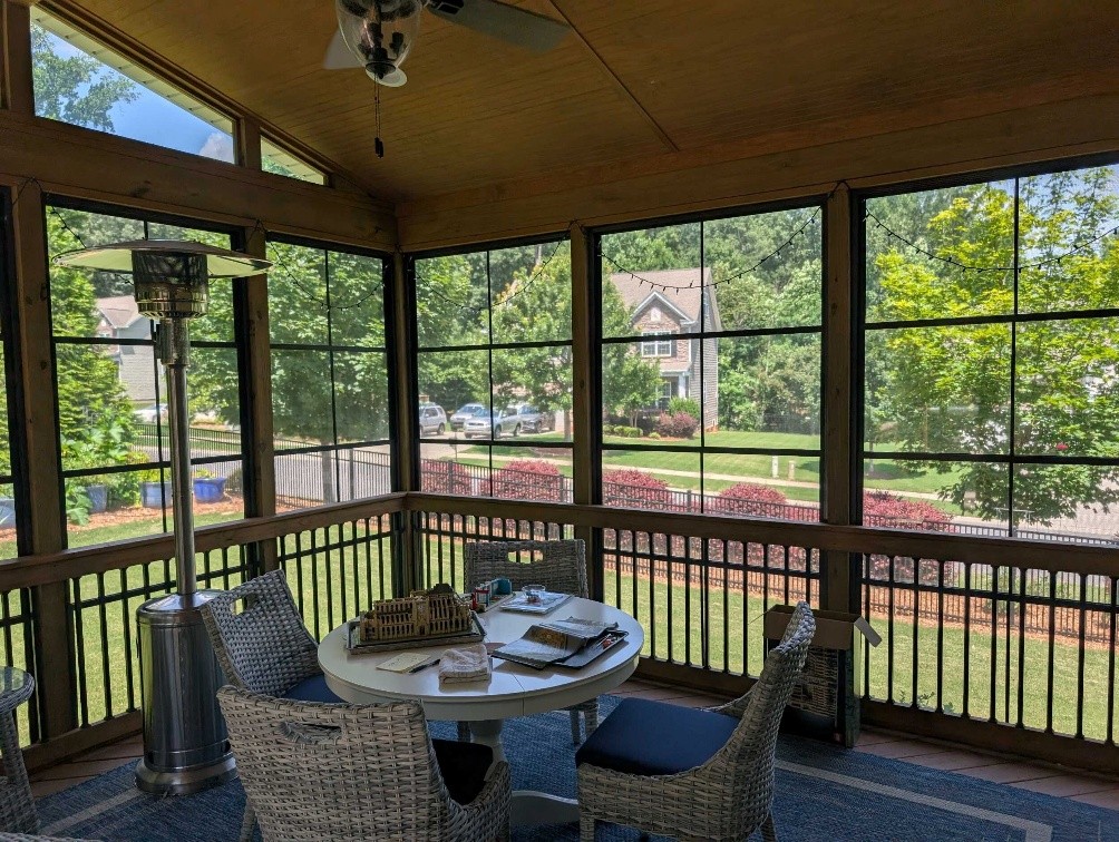 Inside of a custom 3-season room with 4-track windows overlooking suburban summer neighborhood. 
